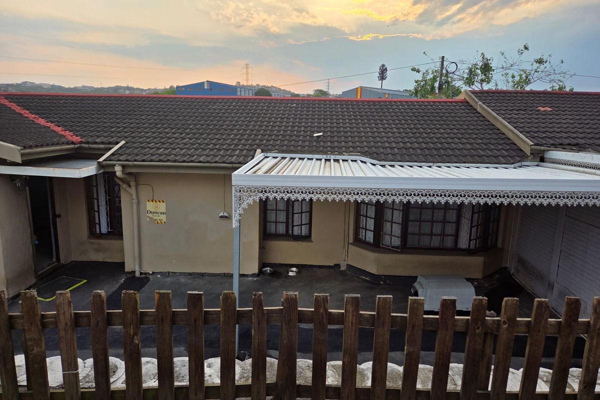 Rear exterior view of a townhouse featuring a tiled roof, a covered patio with decorative metal trim, and a wooden picket fence.