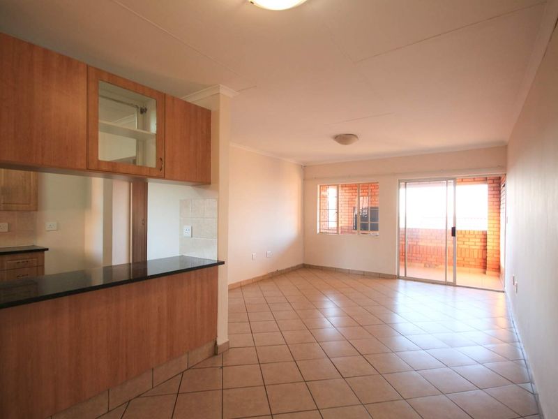 An open-plan living and kitchen area featuring tiled flooring, wooden cabinetry with granite countertops, and sliding glass doors leading to a balcony.