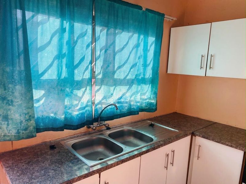 A functional kitchen area featuring a double bowl stainless steel sink, laminate countertops, and white cabinetry with visible signs of wear.