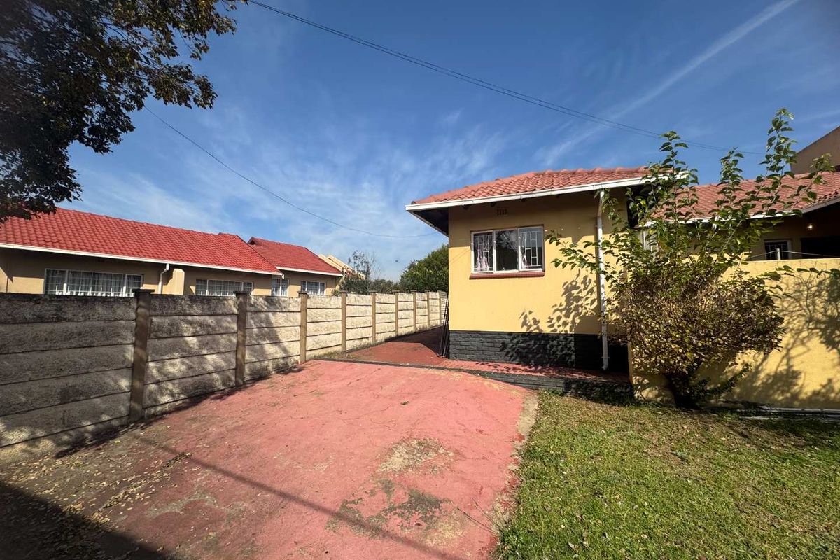 Exterior view of the property featuring a paved driveway, perimeter concrete walling, and a tiled roof structure.