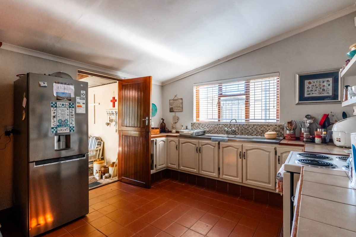 A functional kitchen featuring tiled flooring, built-in cabinetry, a double sink, and a window with blinds, providing direct access to an adjacent room.