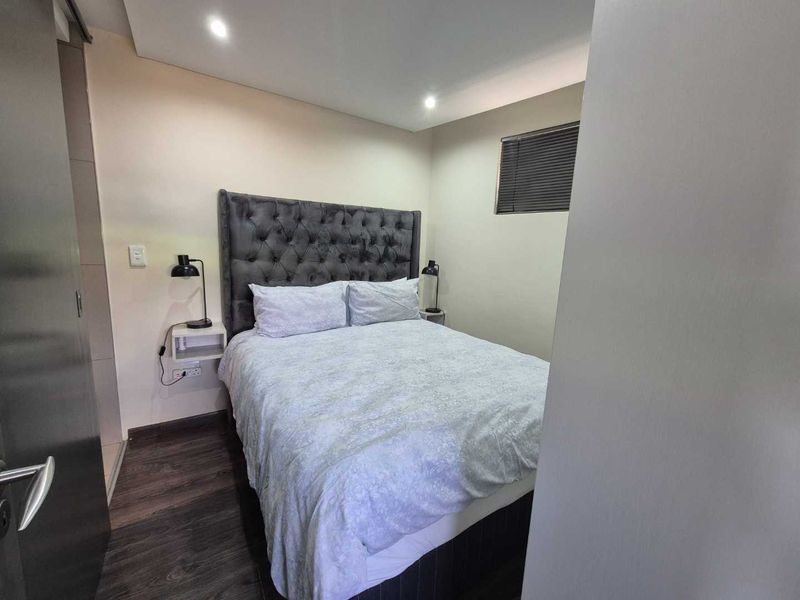 A well-maintained bedroom featuring modern laminate flooring, recessed downlighting, and a functional window with venetian blinds.
