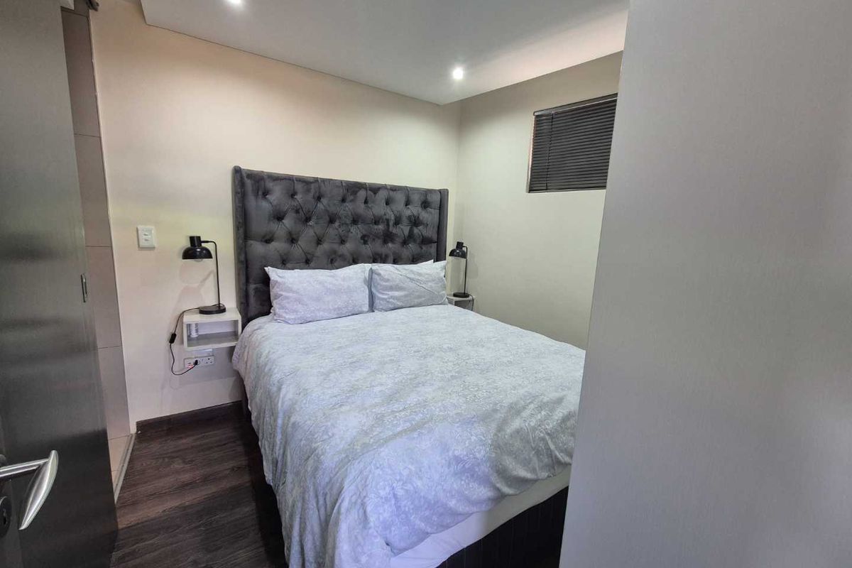 A well-maintained bedroom featuring modern laminate flooring, recessed downlighting, and a functional window with venetian blinds.