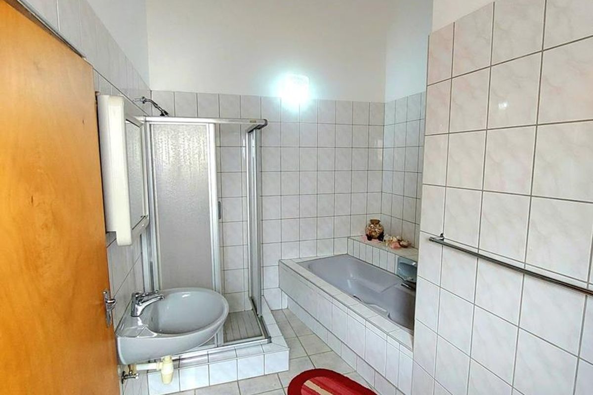 A functional bathroom featuring a built-in bathtub, separate shower enclosure, and wall-mounted basin with exposed plumbing, finished with neutral ceramic tiling.