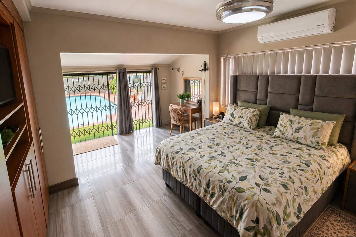 Spacious bedroom featuring tiled flooring, built-in cabinetry, a wall-mounted air conditioning unit, and direct access to the pool area through security gates.