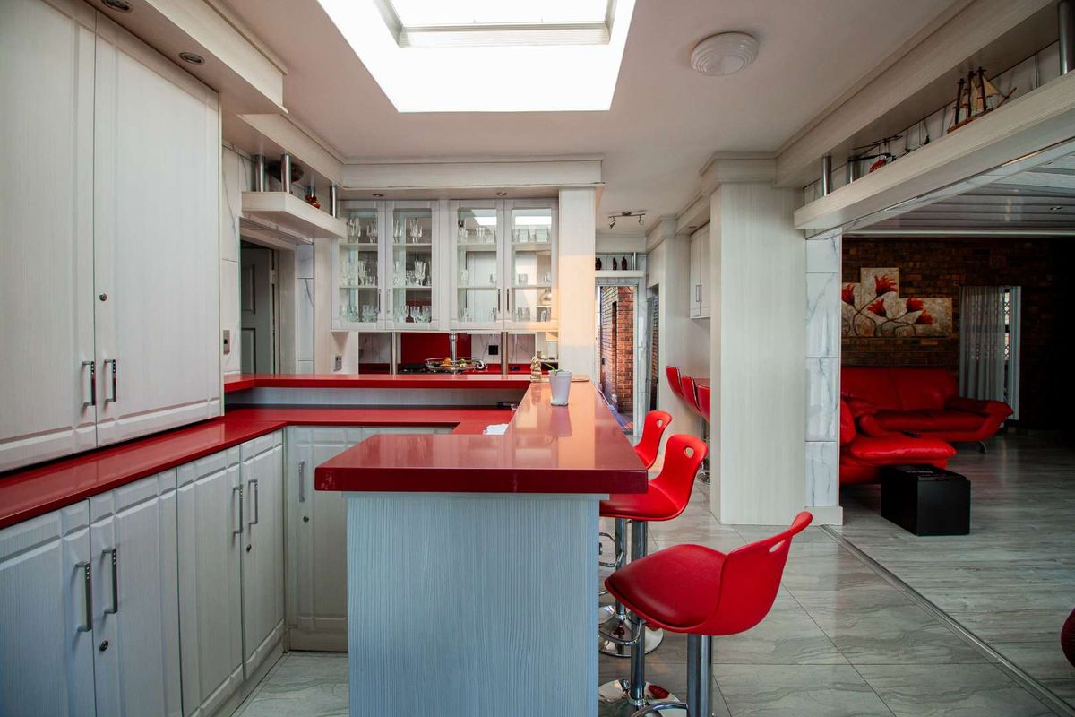A kitchen area featuring a breakfast bar with red countertops, white cabinetry, glass-fronted display cabinets, and a skylight providing natural light.