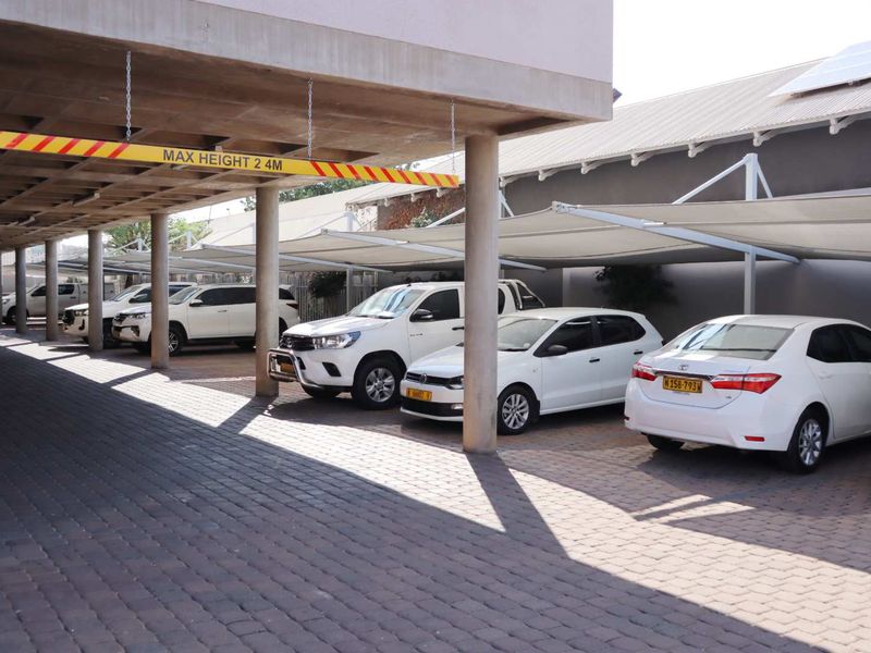 Covered parking area featuring paved ground, concrete support columns, and shade cloth structures for vehicle protection.