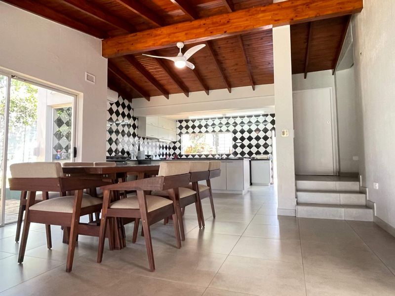 Open-plan living and kitchen area featuring exposed timber ceiling beams, a distinctive checkered tile backsplash, and direct access to the patio through sliding doors.