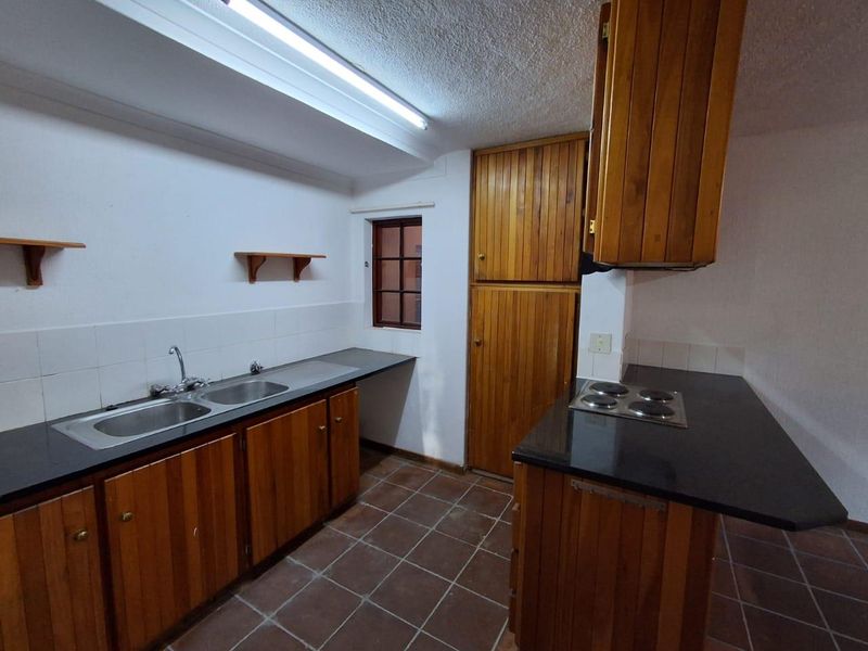 A functional kitchen featuring wooden cabinetry, a double basin sink, built-in hob, and tiled flooring, offering a classic layout ready for modernization.
