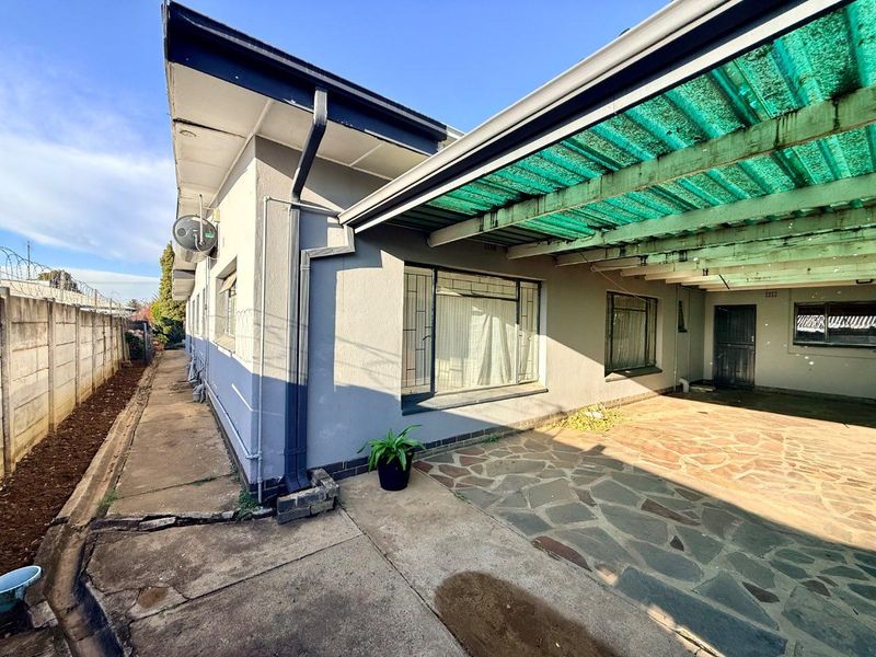Rear exterior view of the property featuring a covered patio area with crazy paving, security bars on windows, and a perimeter wall with razor wire.