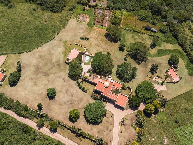 Aerial view of a small holding property featuring multiple detached buildings, a swimming pool, extensive grounds, and a paved driveway.