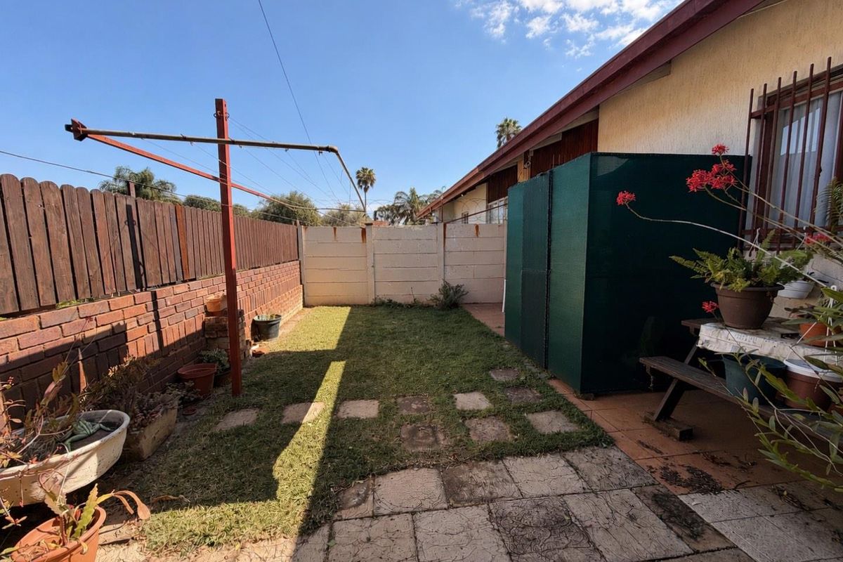 A rear garden area featuring a paved patio, lawn, rotary clothesline, and a mix of brick and precast concrete boundary walls.