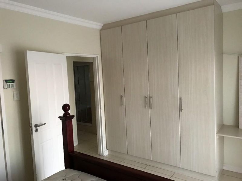 A bedroom featuring light-toned built-in cupboards, tiled flooring, and decorative coving, with an adjacent en-suite bathroom visible through the doorway.