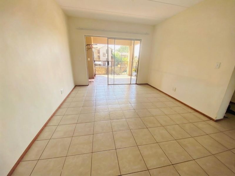 An empty, open-plan living area featuring neutral tiled flooring and a sliding glass door providing access to an outdoor balcony.