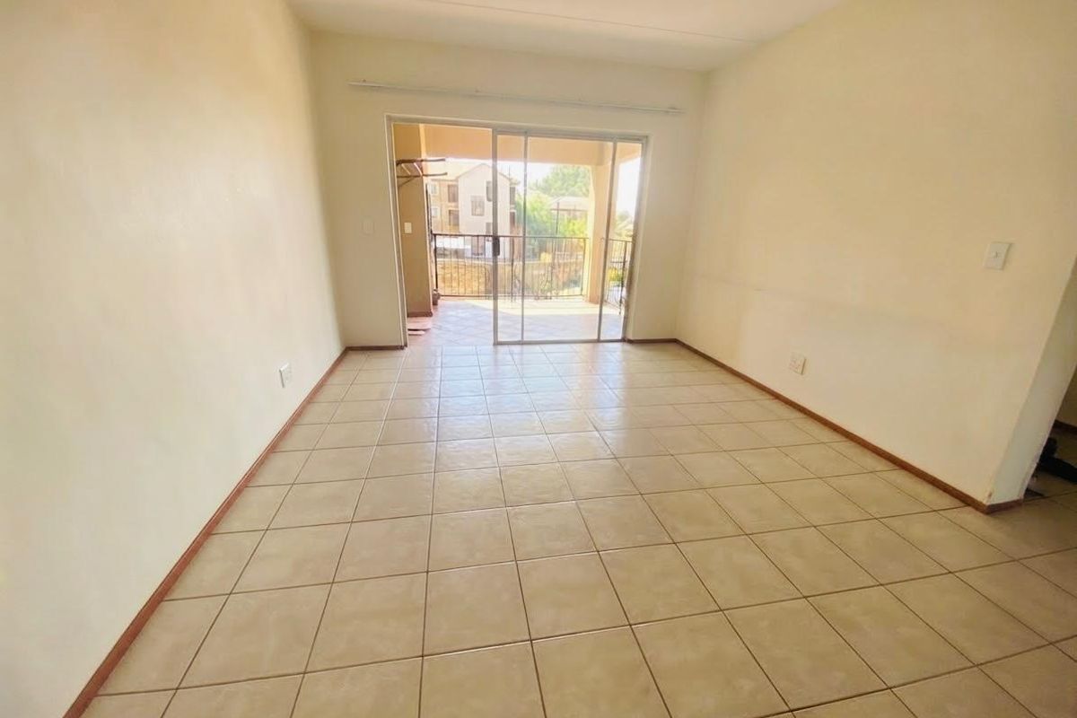 An empty, open-plan living area featuring neutral tiled flooring and a sliding glass door providing access to an outdoor balcony.