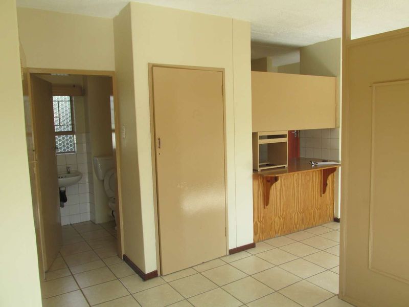An open-plan living area featuring tiled floors, a dated kitchen with breakfast bar, and an adjacent bathroom with basic fixtures.
