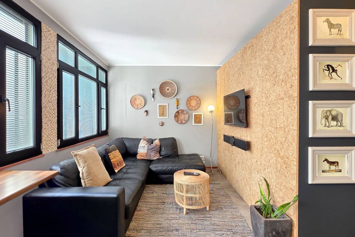 A modern living room featuring a unique cork-paneled feature wall, black aluminum window frames, and neutral grey tones.