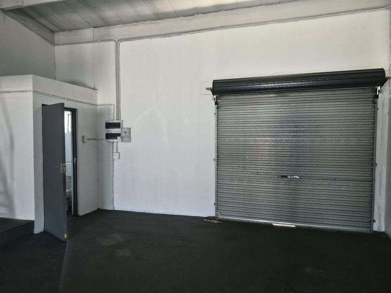 Industrial garage space featuring a large roller shutter door, exposed electrical conduit, and concrete flooring, suitable for storage or workshop use.