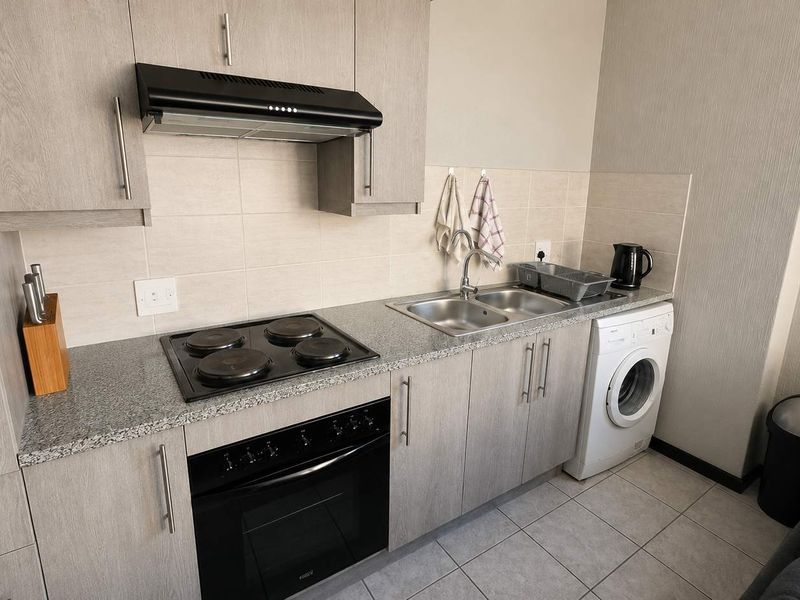 Compact modern kitchen featuring light wood-grain cabinetry, granite countertops, built-in electric oven and hob, extractor fan, and integrated laundry plumbing.