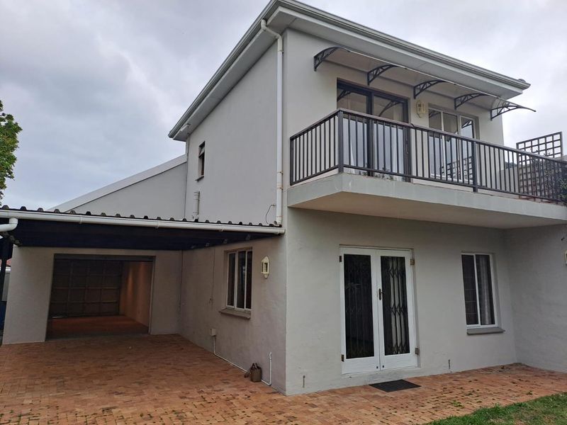 Rear view of the cottage featuring a paved patio area, a covered carport, and an upper-level balcony with metal railings.