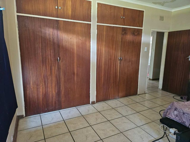 Bedroom featuring tiled flooring and extensive built-in wooden cupboards, showing signs of ceiling water damage and wear.