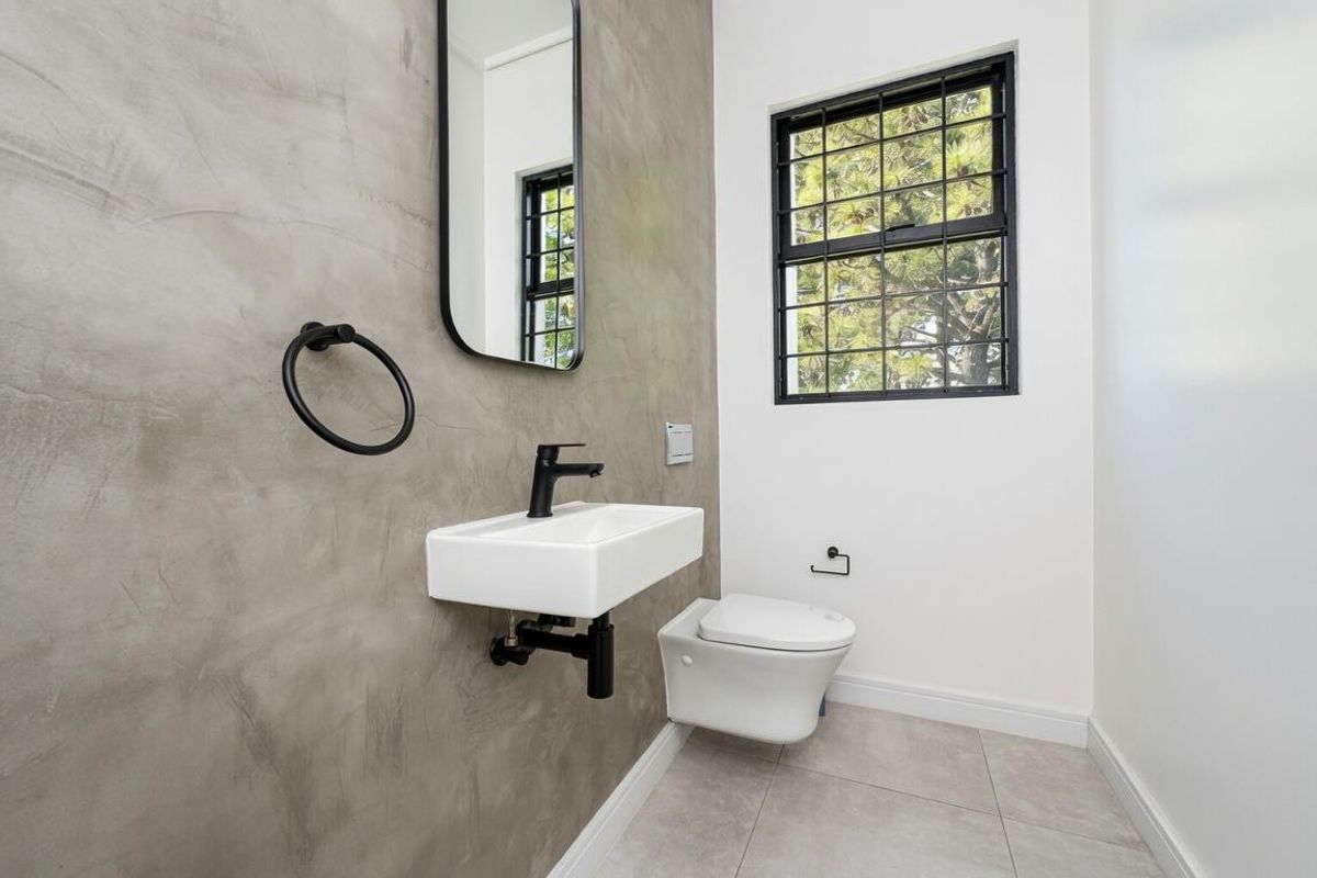 Modern guest bathroom featuring a wall-mounted basin, sleek black fixtures, a contemporary toilet, and a feature wall with a polished concrete finish.