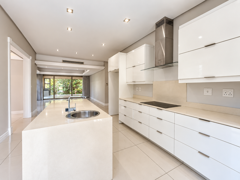 Modern, spacious kitchen featuring a large island with stone countertops, sleek white cabinetry, integrated hob, and stainless steel extractor fan, finished with polished floor tiles.