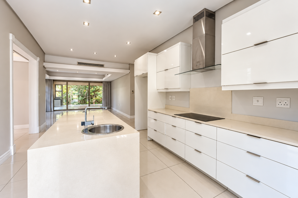 Modern, spacious kitchen featuring a large island with stone countertops, sleek white cabinetry, integrated hob, and stainless steel extractor fan, finished with polished floor tiles.
