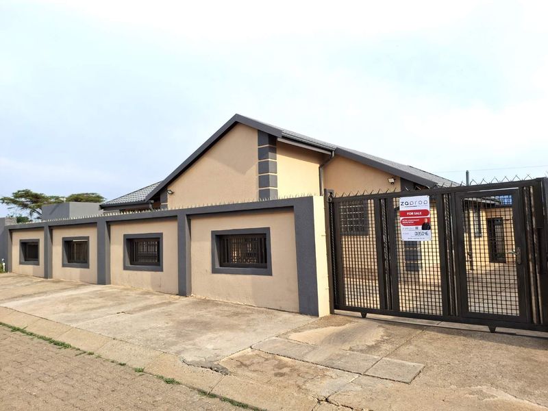 Front exterior view of the house featuring a secure perimeter wall, metal gate, security spikes, and a concrete driveway.