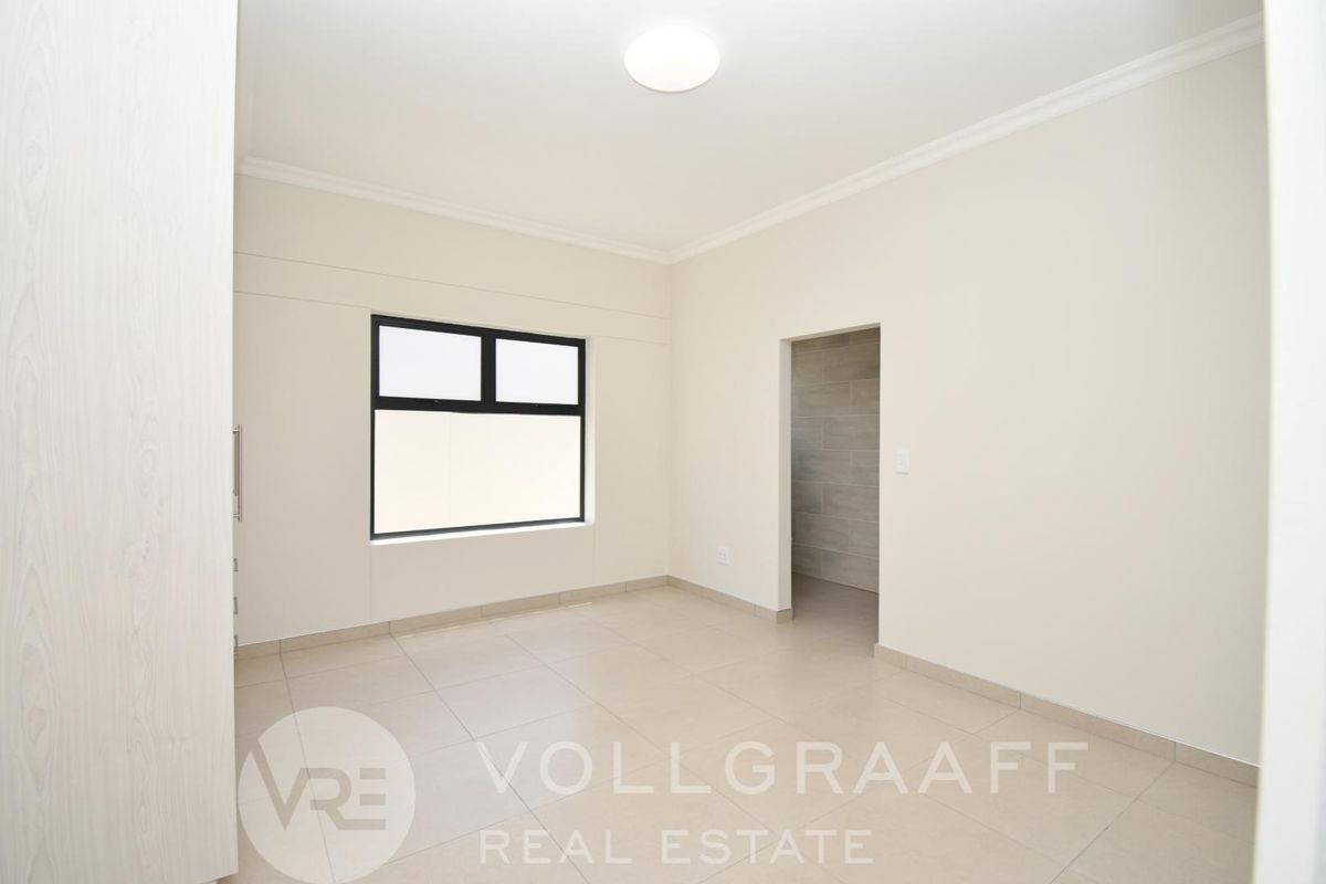 A bright, empty bedroom featuring neutral tiled flooring, modern black-framed windows, and clean white walls, offering a versatile space ready for personalization.