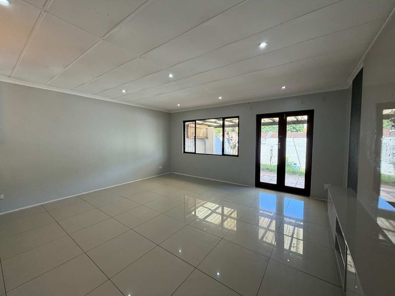 Spacious, empty living room featuring polished tiled flooring, recessed downlights, and direct access to the outdoor area through double glass doors.