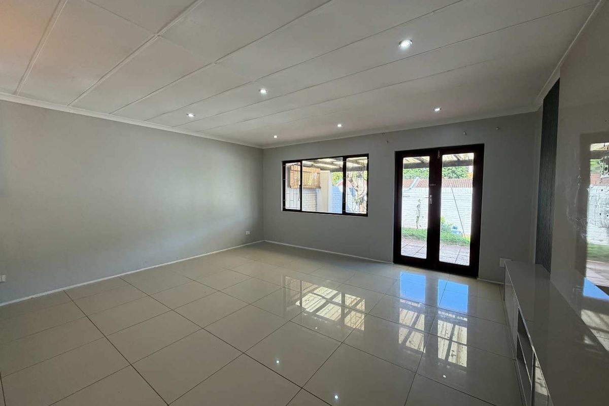 Spacious, empty living room featuring polished tiled flooring, recessed downlights, and direct access to the outdoor area through double glass doors.