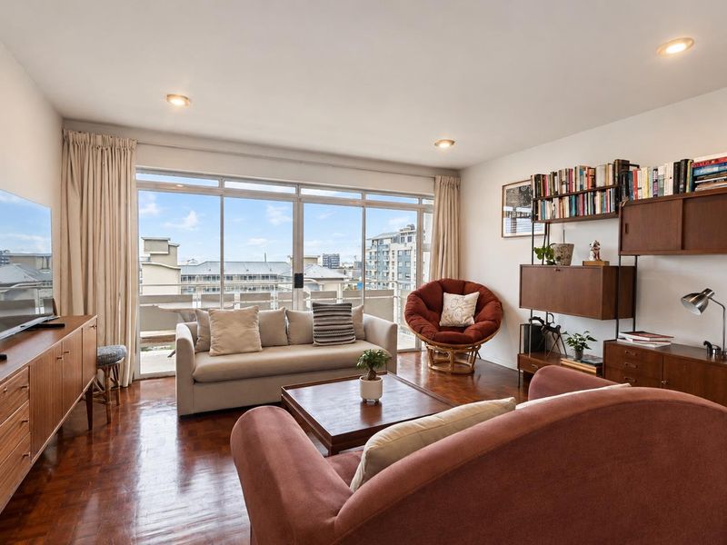A bright living room featuring warm parquet flooring, recessed lighting, and large sliding glass doors that open to a balcony with city views.