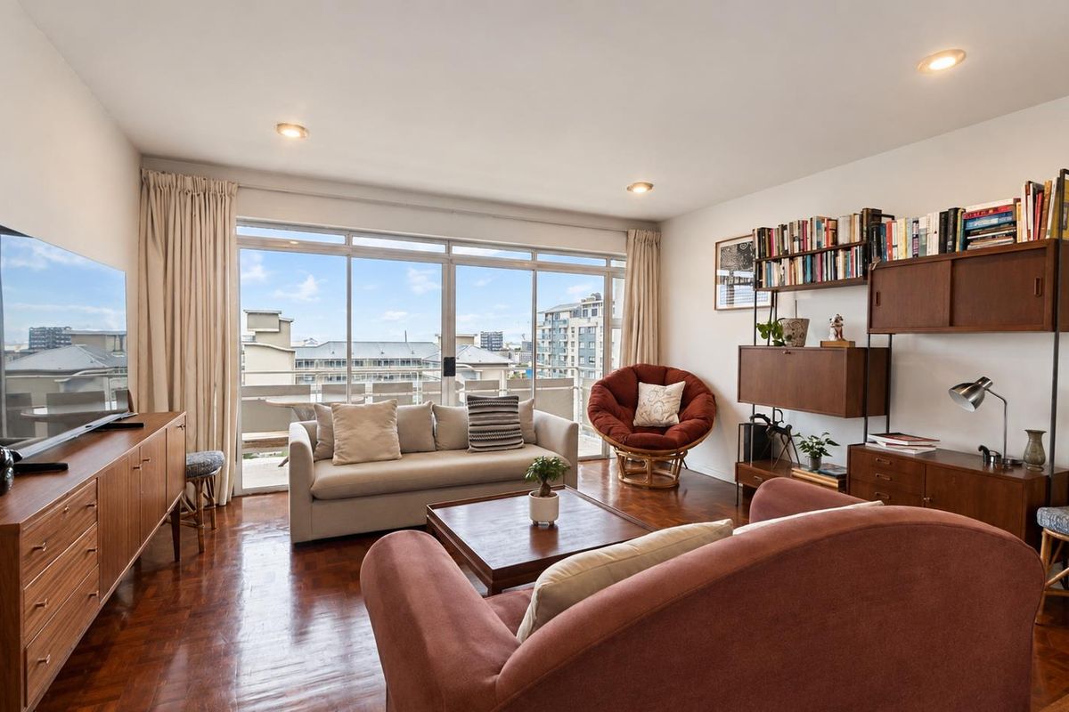 A bright living room featuring warm parquet flooring, recessed lighting, and large sliding glass doors that open to a balcony with city views.