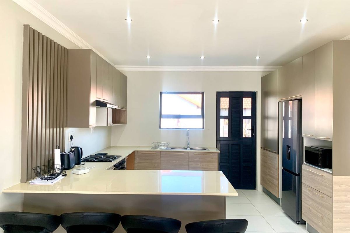Modern kitchen featuring sleek built-in cabinetry, stone countertops, a gas hob with extractor, and integrated appliances, finished with clean tiled flooring and recessed lighting.