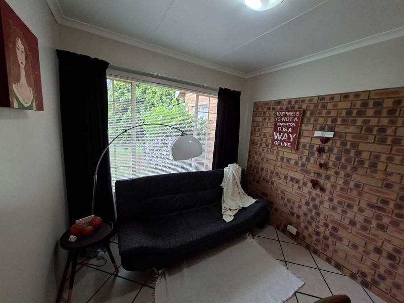 A cozy living room featuring an exposed brick accent wall, tiled flooring, and a large window providing natural light.
