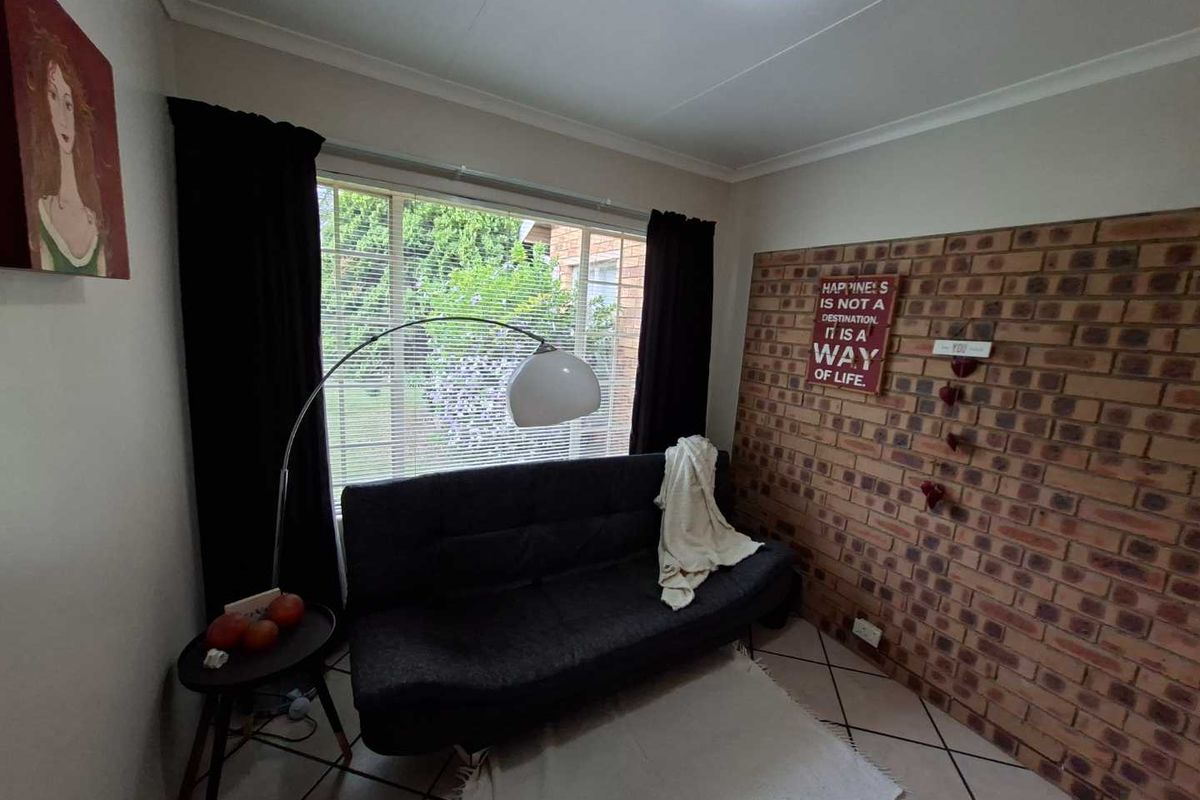 A cozy living room featuring an exposed brick accent wall, tiled flooring, and a large window providing natural light.