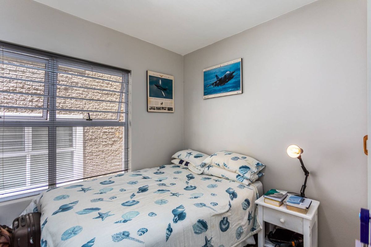 A functional bedroom featuring a large window with fitted blinds, providing natural light and a neutral wall finish.