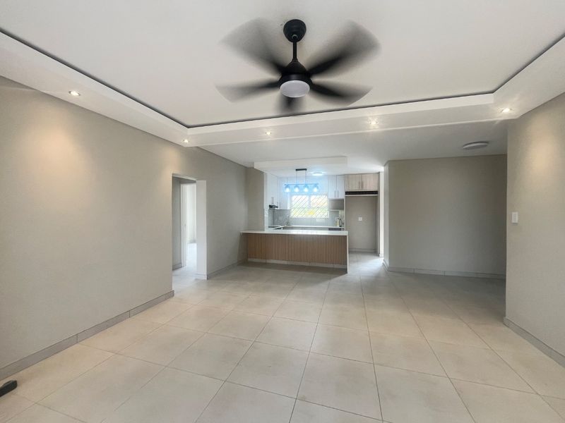 Spacious open-plan living area featuring modern tiled flooring, recessed lighting, a ceiling fan, and a contemporary kitchen with built-in cabinetry and island.
