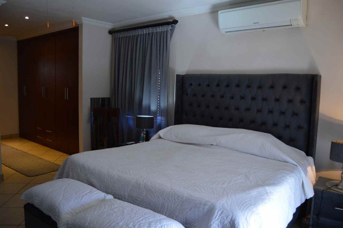A well-maintained bedroom featuring built-in cupboards, tiled flooring, and a wall-mounted split-system air conditioner.