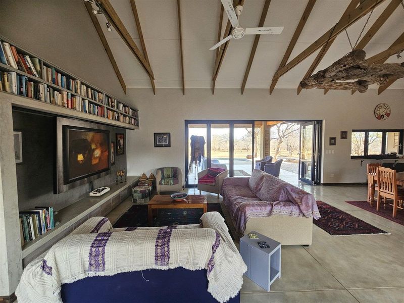 Spacious open-plan living area featuring vaulted ceilings with exposed timber rafters, polished concrete floors, and large stacking doors opening to the outdoor patio.