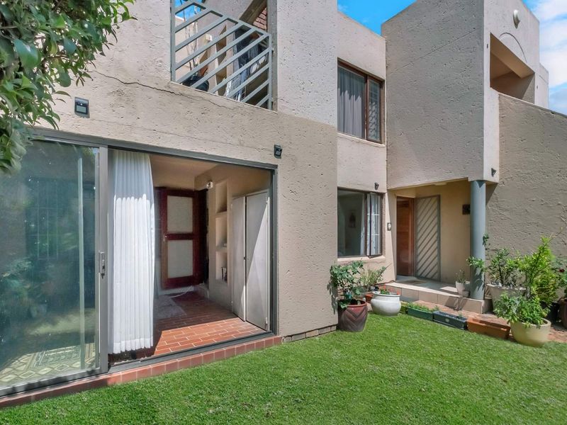 Rear view of the apartment featuring a private garden, terracotta tiled patio, and sliding glass doors leading into the living area.