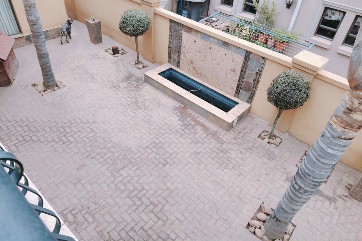 A paved rear courtyard featuring a built-in water feature, boundary walls, and established palm trees, providing a low-maintenance outdoor space.