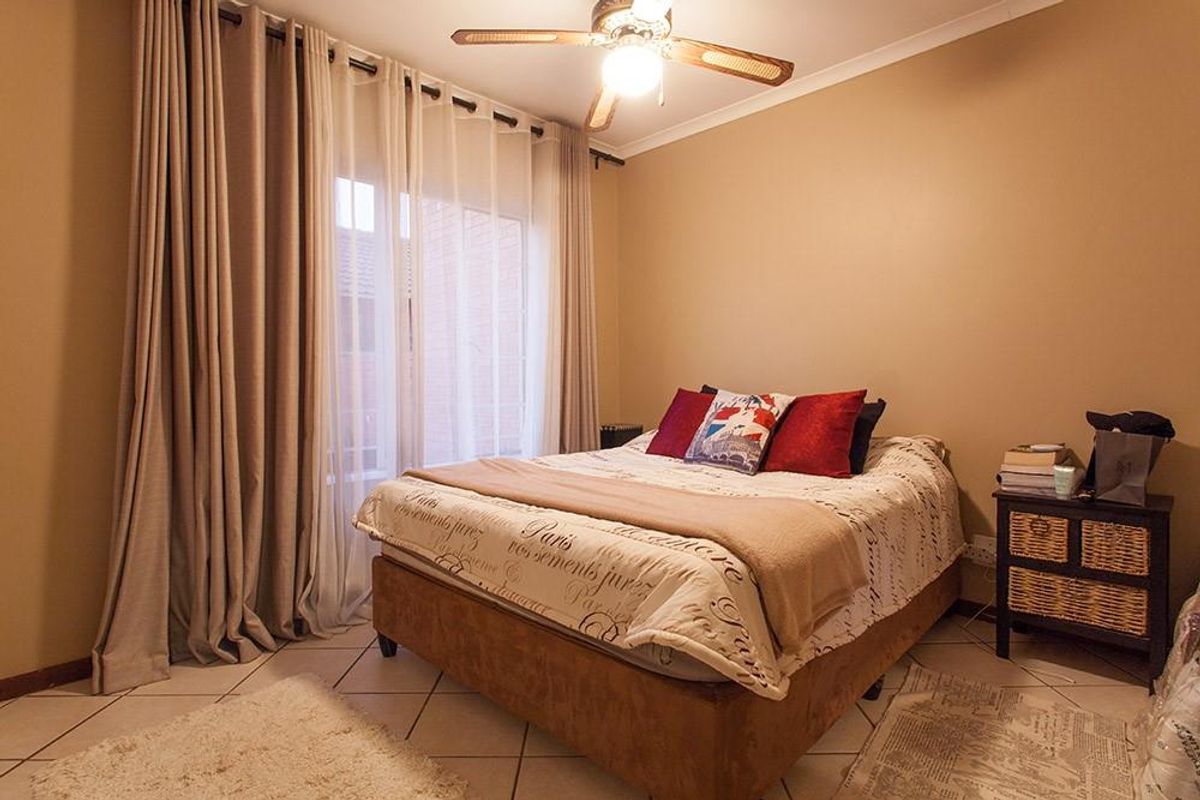 A well-lit bedroom featuring tiled flooring, a ceiling fan, and large sliding glass doors with curtains providing access to the exterior.