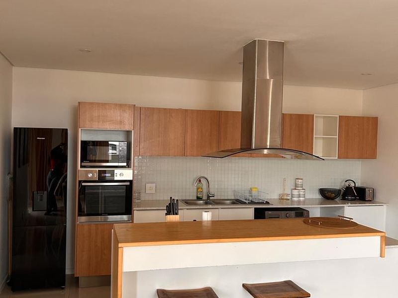 Modern kitchen featuring wood-finish cabinetry, a central island with breakfast bar, built-in appliances, and a stainless steel extractor fan.