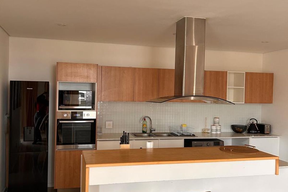 Modern kitchen featuring wood-finish cabinetry, a central island with breakfast bar, built-in appliances, and a stainless steel extractor fan.