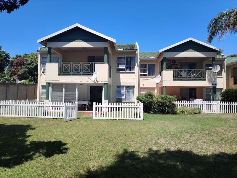 Rear view of a two-story apartment complex featuring private balconies, ground-floor patios with picket fencing, and a shared garden area.