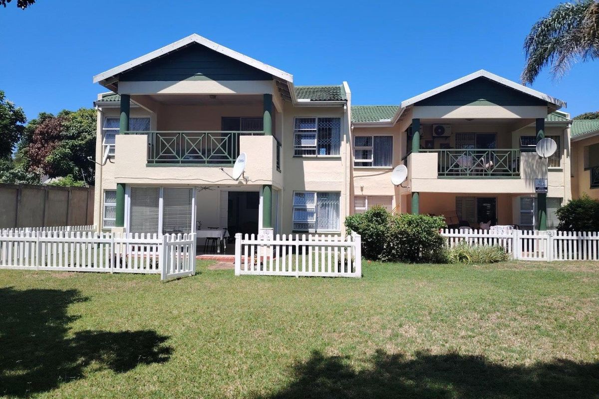 Rear view of a two-story apartment complex featuring private balconies, ground-floor patios with picket fencing, and a shared garden area.
