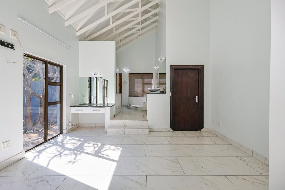 Spacious bedroom featuring vaulted ceilings, marble-look tiled flooring, a built-in vanity area, and an en-suite bathroom with a raised platform.