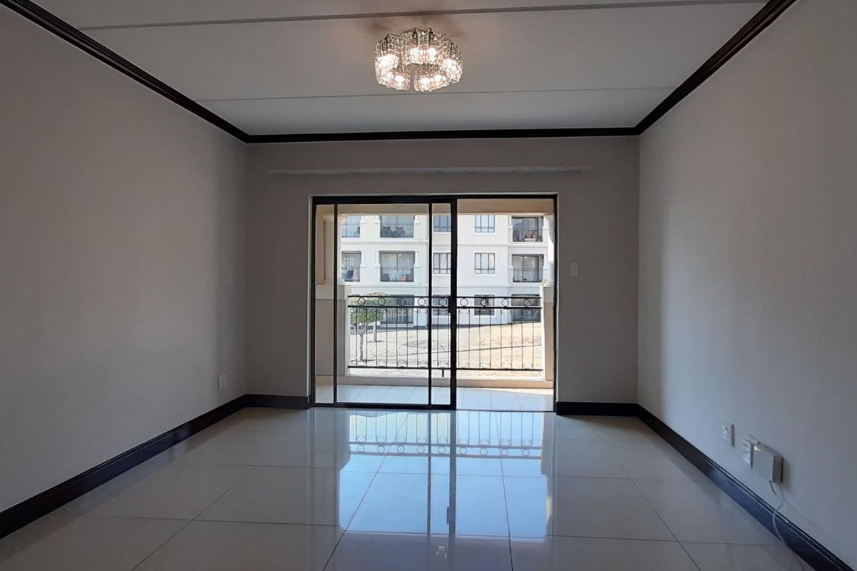 A bright, empty living room featuring polished porcelain floor tiles, dark skirting boards, and a sliding glass door leading to a balcony.